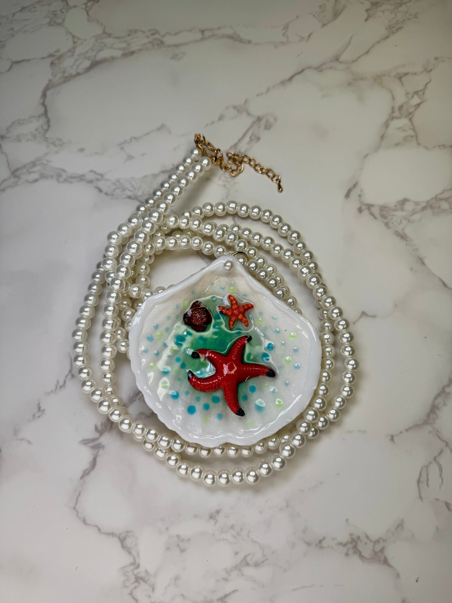 Starfall Lagoon Natural seashell featuring a large metal handmade craft red starfish, a tiny orange starfish, and blue-green dotted resin accents preserved in UV clear resin . Beautiful extra large glasses necklace