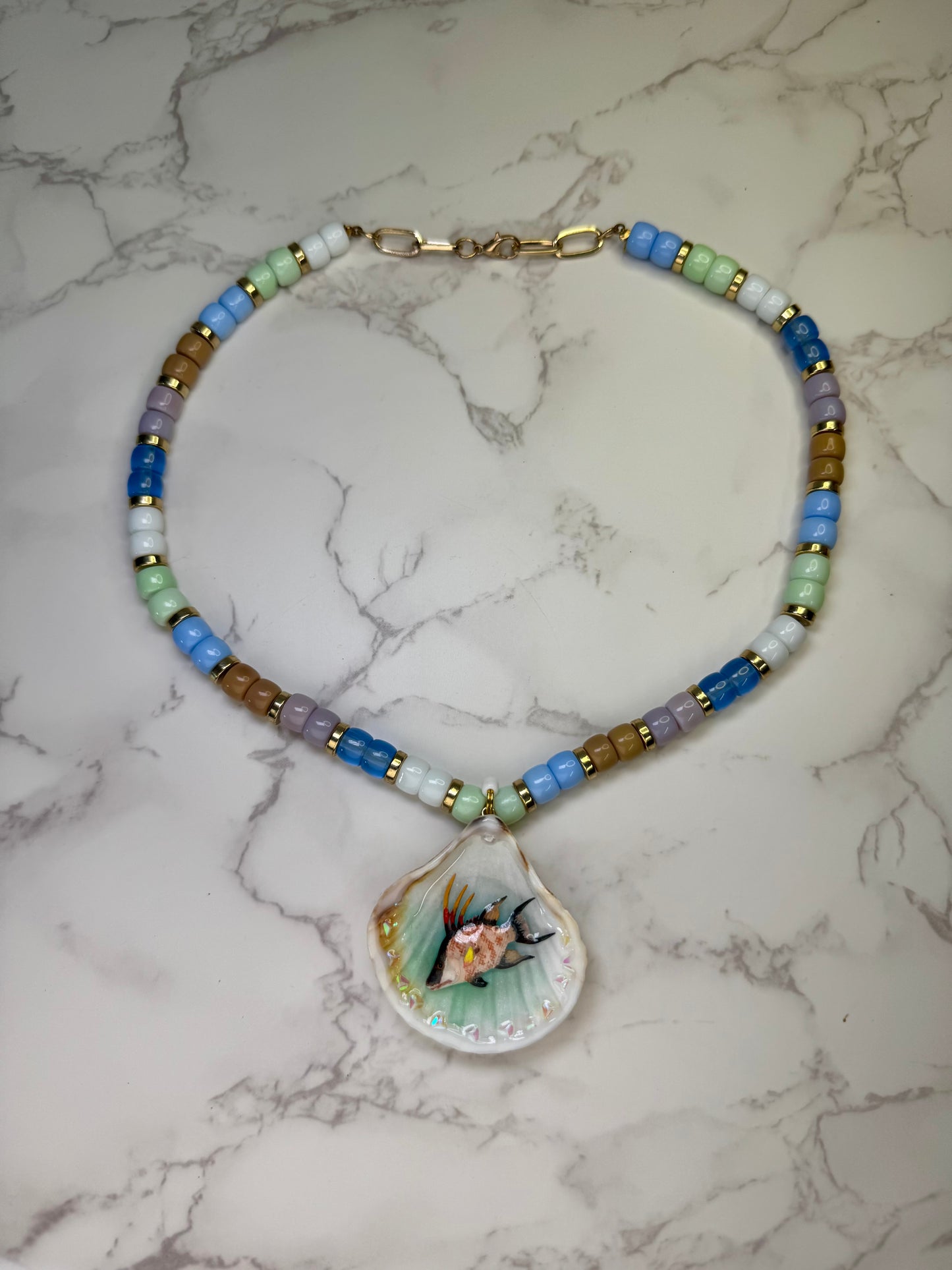 Reef Wanderer Natural seashell featuring a miniature hogfish and a beaded necklace in blue, white, green, and purple encapsulated in clear UV resin