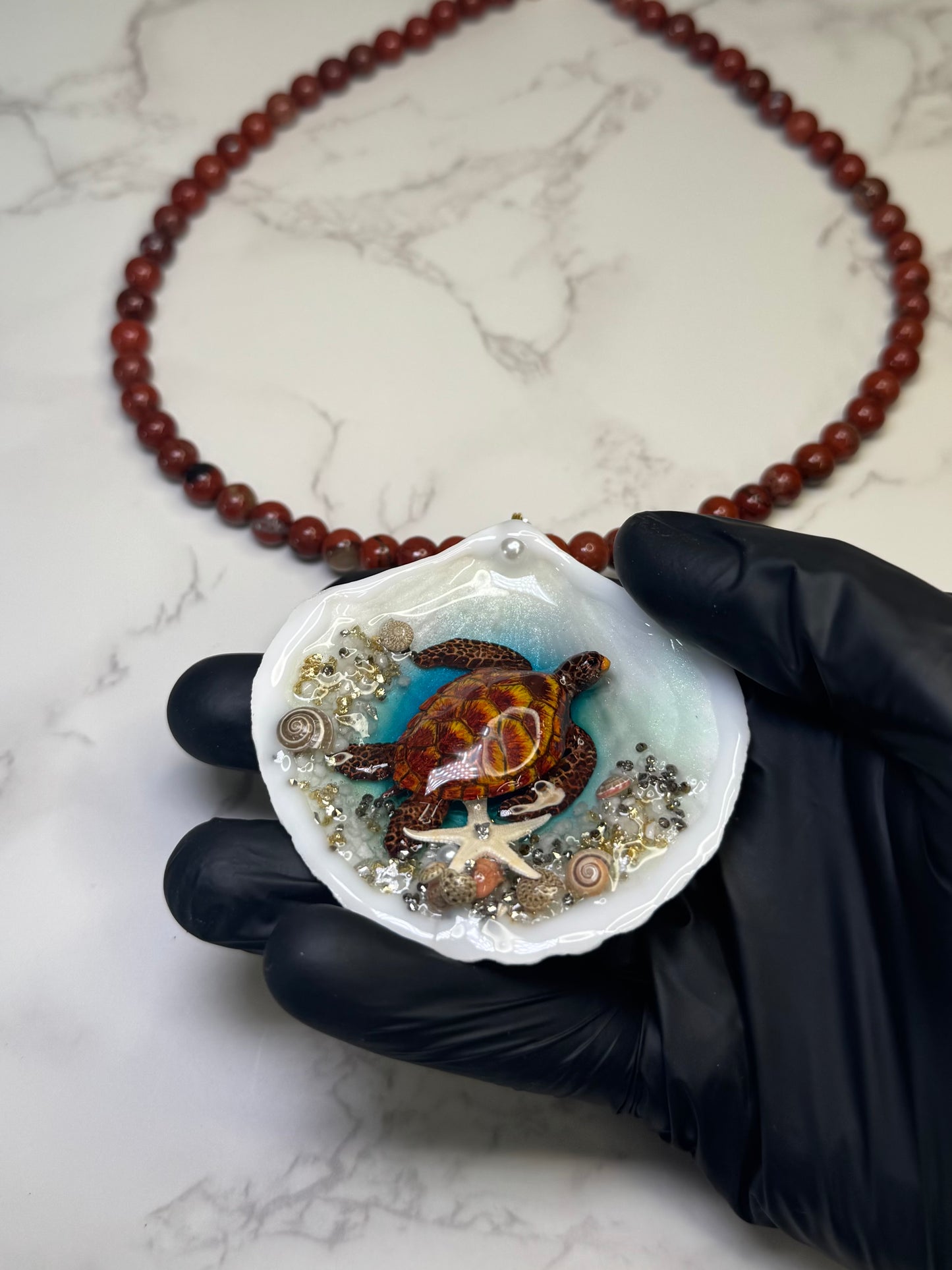 Golden Ember Current Natural seashell featuring a beautiful metal handmade metal brown-and-yellow sea turtle, sand, golden sparkles, seashells, and a tiny starfish, preserved in clear UV resin paired with a crimson crystal ball necklace