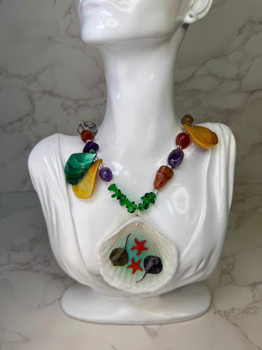 Coral Sky Drift Natural seashell featuring two tiny red starfish and miniature stingrays, paired with a colorful coral-and-glass-rock necklace in green, orange, red, and purple