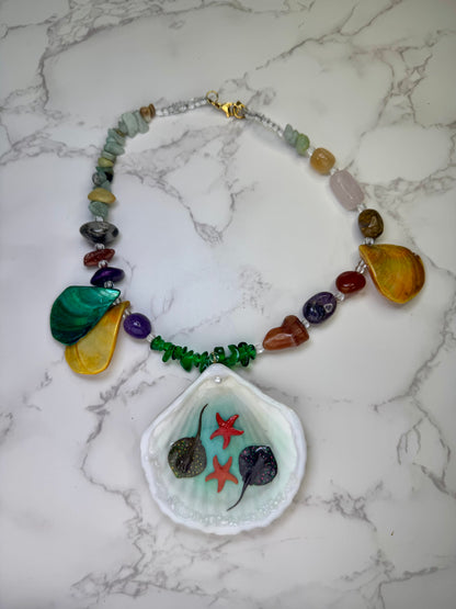 Coral Sky Drift Natural seashell featuring two tiny red starfish and miniature stingrays, paired with a colorful coral-and-glass-rock necklace in green, orange, red, and purple