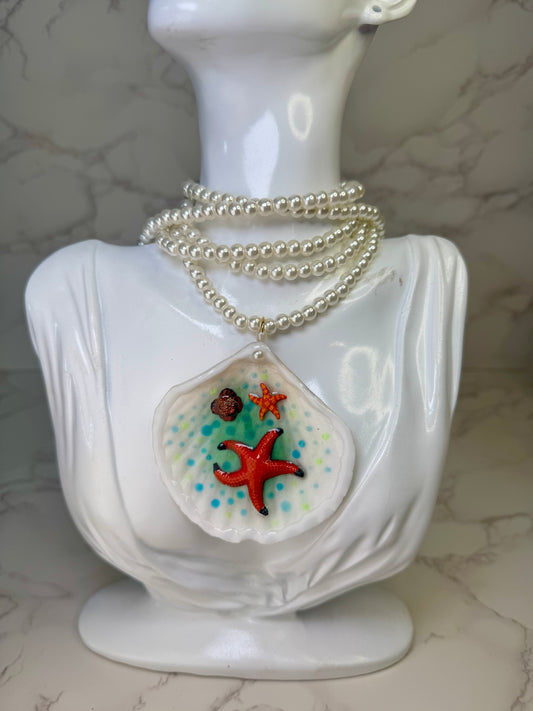 Starfall Lagoon Natural seashell featuring a large metal handmade craft red starfish, a tiny orange starfish, and blue-green dotted resin accents preserved in UV clear resin . Beautiful extra large glasses necklace