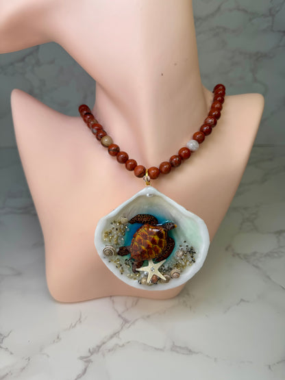 Golden Ember Current Natural seashell featuring a beautiful metal handmade metal brown-and-yellow sea turtle, sand, golden sparkles, seashells, and a tiny starfish, preserved in clear UV resin paired with a crimson crystal ball necklace
